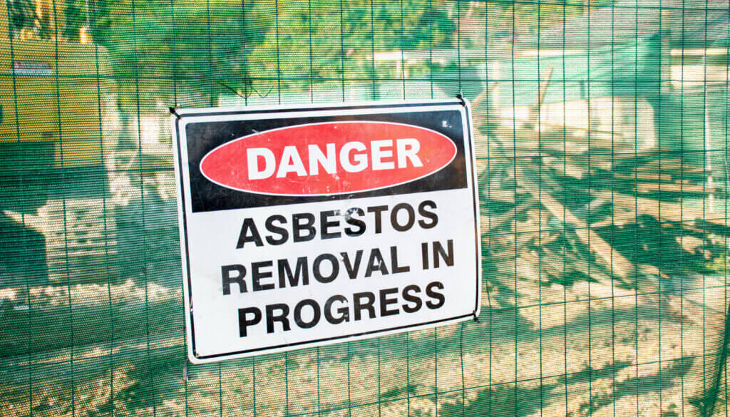 a job site undergoing commercial asbestos abatement is fenced off with a danger sign notifying removal is in progress
